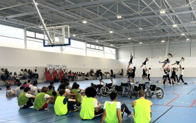 Personnes en dossard dans un gymnase regardant un spectacle de cheerleaders, des fauteuils roulants sont également disposés